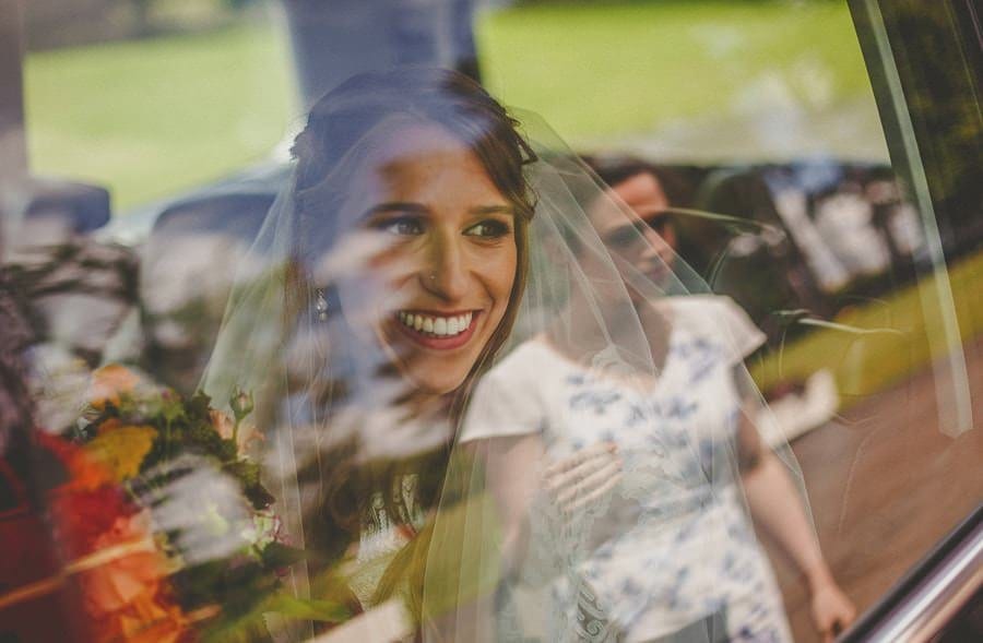 The bride looks out of the car window and smiles at one of the bridesmaids