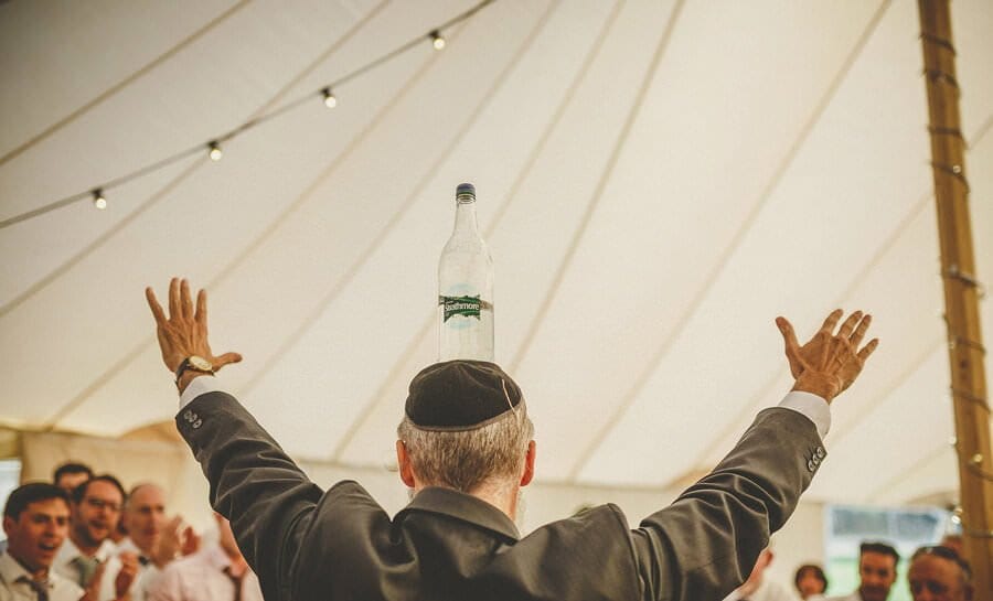 A jewish man balances a bottle of water on his head in the marquee
