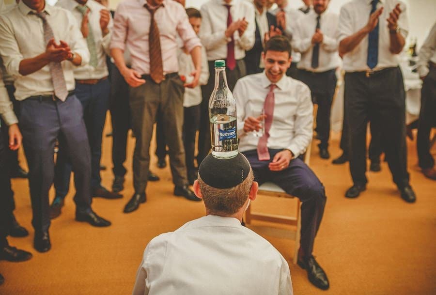 A jewish man faces the groom with a bottle of water on his head