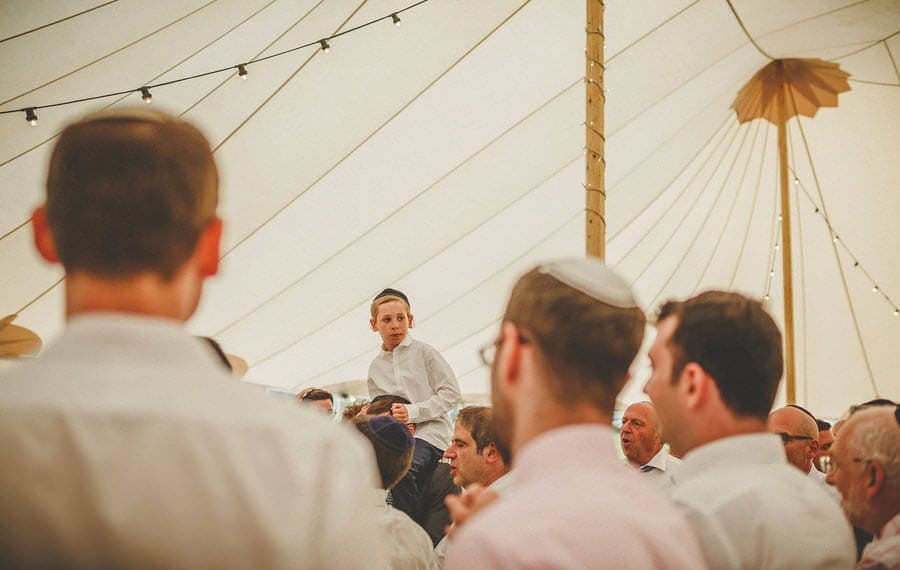 A jewish boy sits on the shoulders of his father on the dancefloor of the marquee