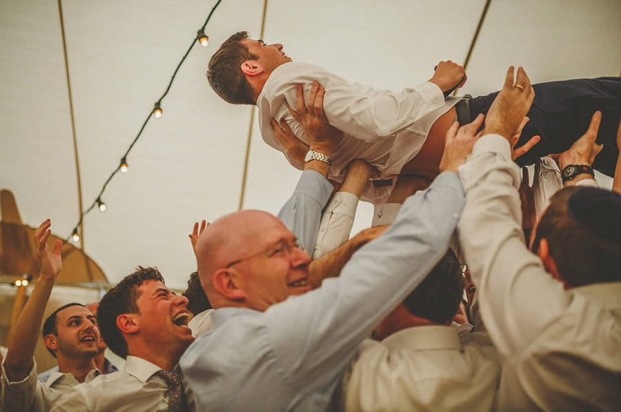 The groom is lifted in the air by men on the dancefloor of the marquee
