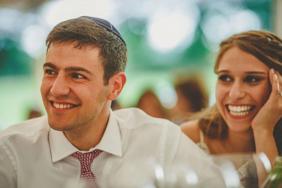 The bride and groom sit at the table and smile as they listen to a speech