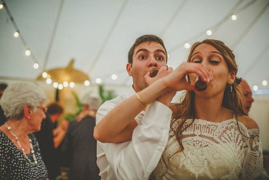 The bride and groom drink a shot of whisky together on the dancefloor in the marquee at Brook farm