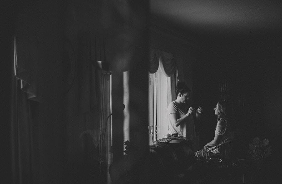 The make up artist next to the window as she puts on make up on one of the bridesmaids