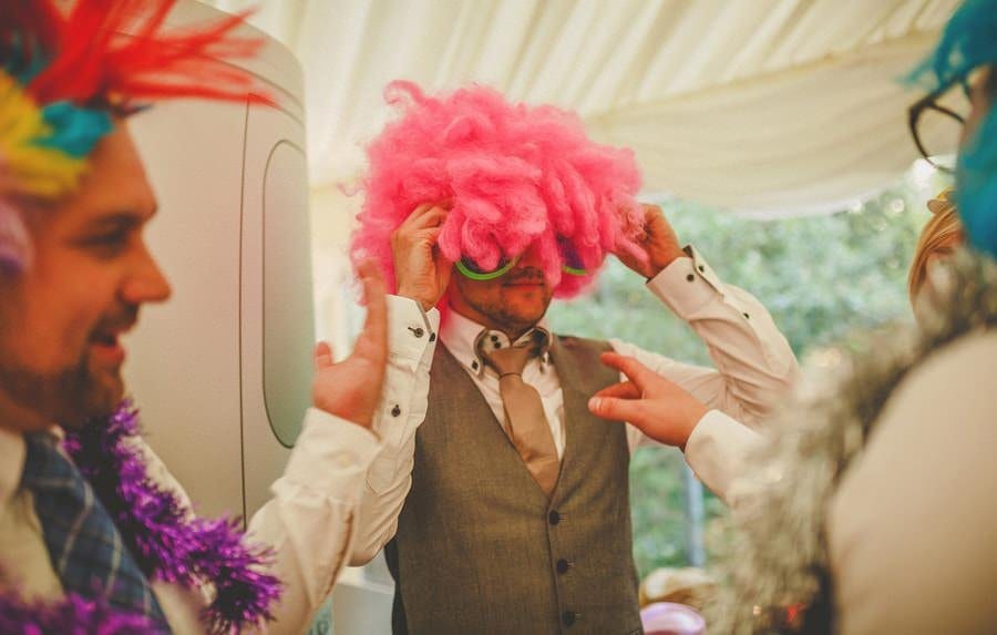 A wedding guest puts on a wig and sunglasses next to the photo booth