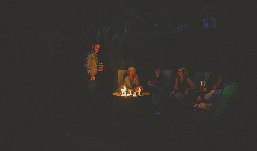 The wedding party sit around an open fire in the garden