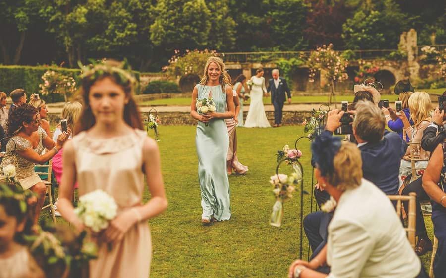 A bridesmaid and flowergirls walk down the aisle of the outdoor ceremony at Voewood