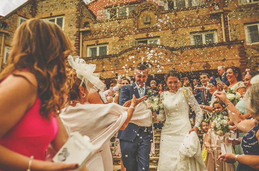The wedding party throw confetti as the bride and groom walk down the stone steps at the front of Voewood