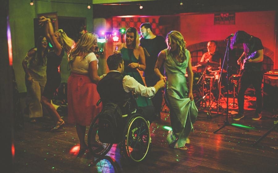 A man in a whellchair dances with a bridesmaid on the dancefloor at Voewood