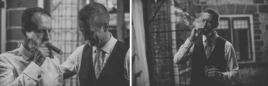 An ushers smokes a cigar as the groom watches and smiles