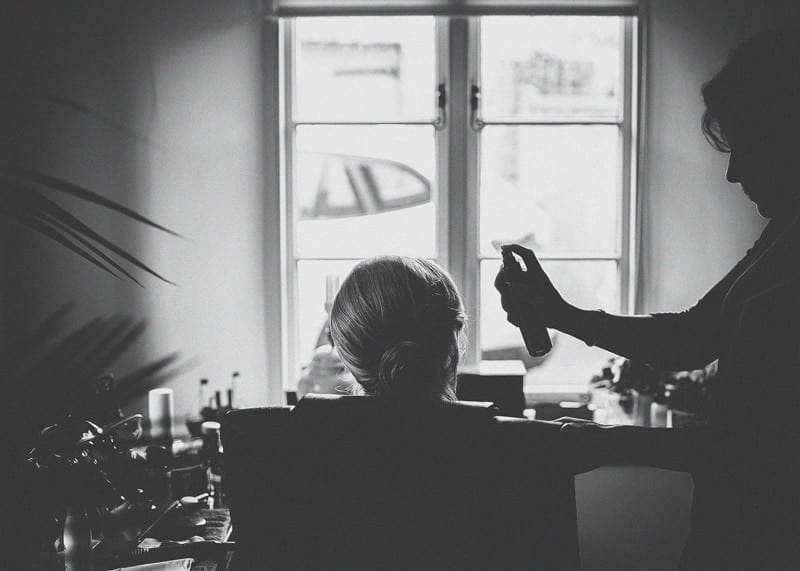 The make up artist sprays hairspray onto a bridesmaids hair