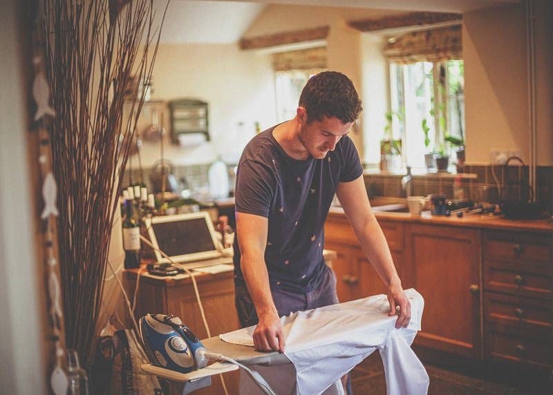 The brides brother irons his shirt in the kitchen