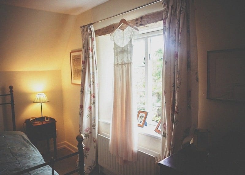The brides dress hangs from the curtain rail of her mothers bedroom