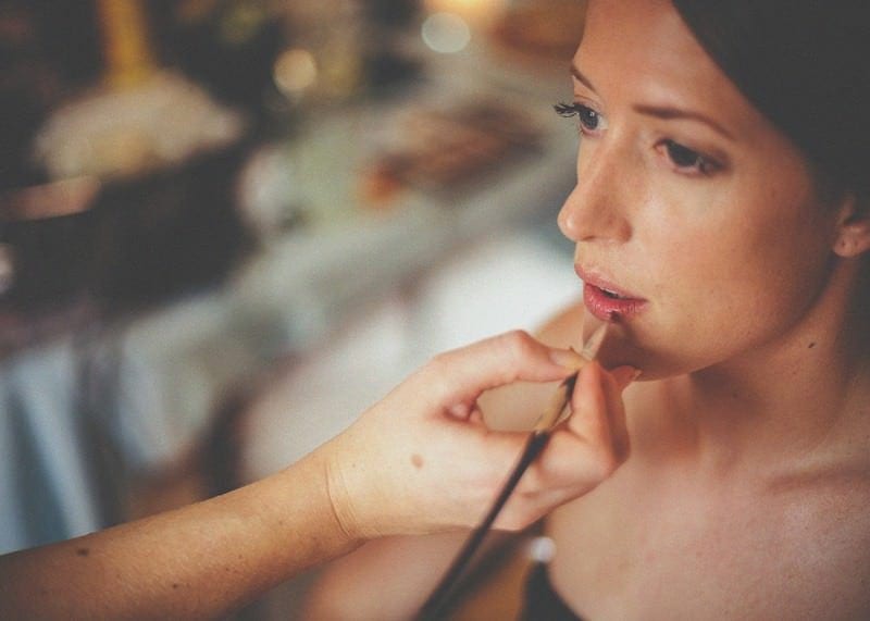 The make up artist applies lipstick to the lips of the bride