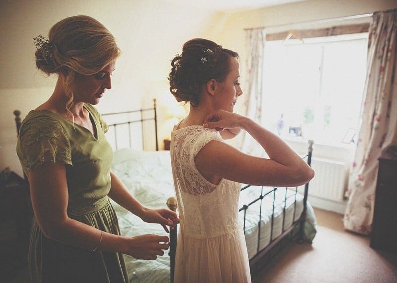 A bridesmaid fastens the back of the brides dress