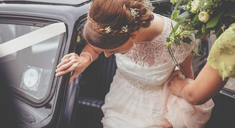 The bride is helped into the car by one of the bridesmaids