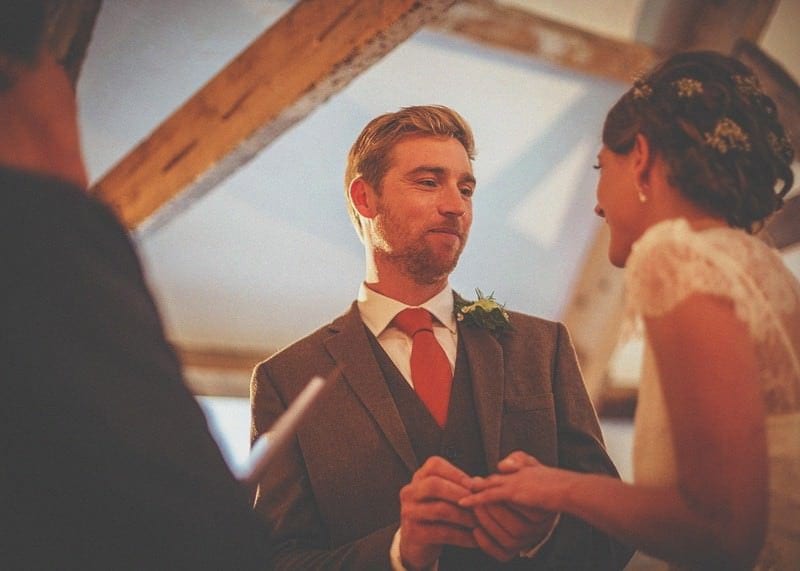 The groom places a ring on the finger of the bride during the wedding ceremony at Almonry Barn