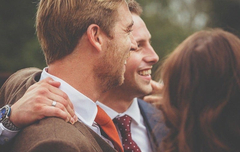 A wedding guest puts his arm around the groom and smiles