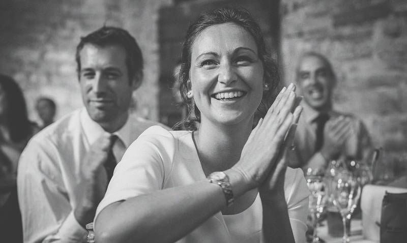 A lady smiles and claps during a wedding speech in the barn
