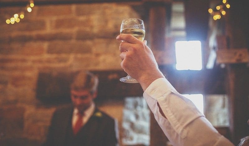 A glass of champagne is raised in the air during a wedding speech in the barn