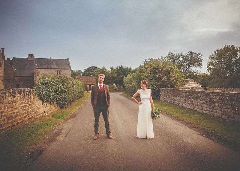 The bride and groom stand in the middle of the road outside Almonry Barn