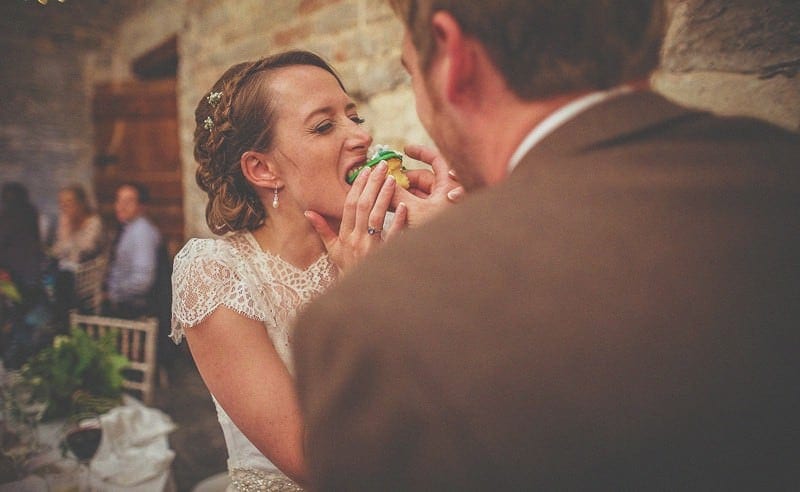 The groom puts a cupcake in the mouth of the bride