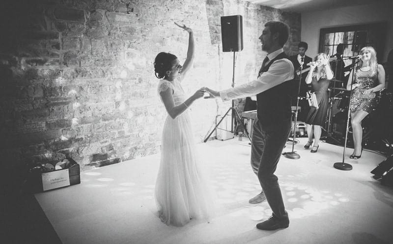 The bride raises her left arm in the air and laughs with the groom on the dancefloor