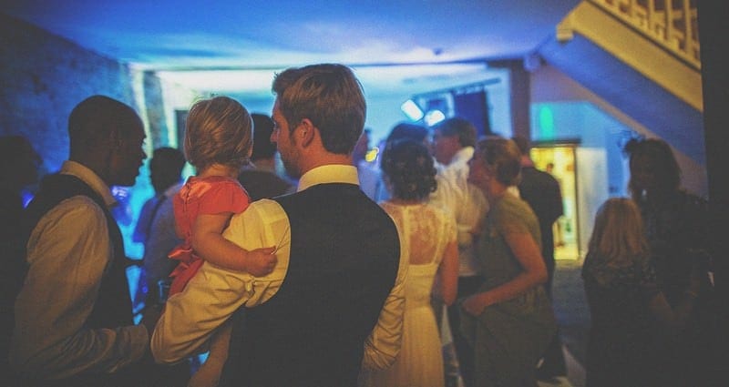 The groom holds a little girl in his arms on the edge of the dancefloor