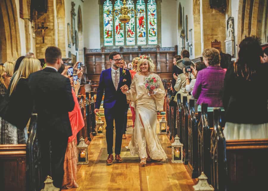 The bride and groom walk down the aisle of the Church of St Michael and All Angels, Somerton