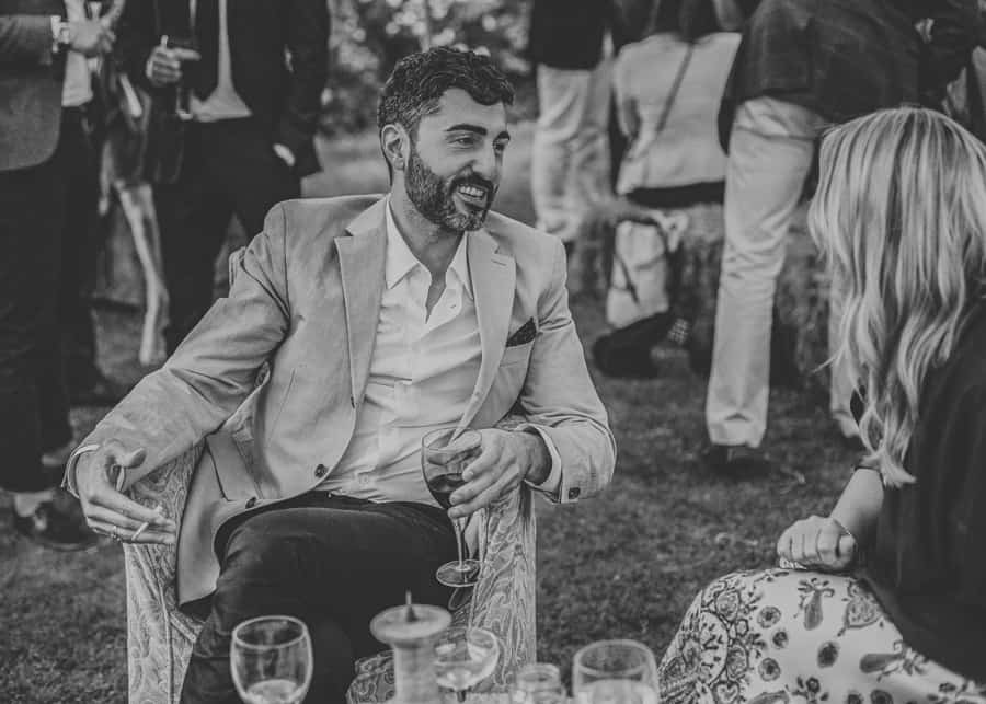 A wedding guest sat with a glass of wine talks to a friend of the bride and groom