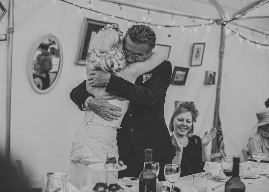 The brides father stands up and embraces his daughter in the marquee at Sharpham Park