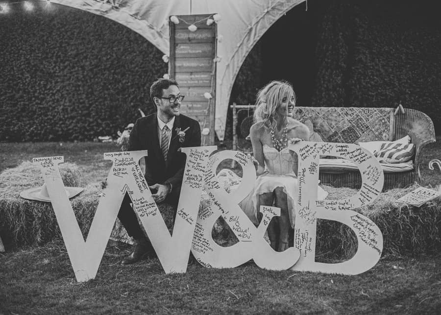 The bride and groom sit on hay bails in the garden at Sharpham Park