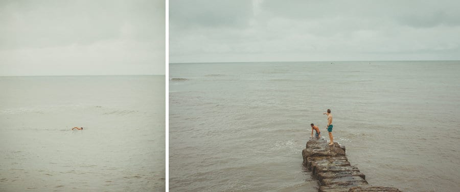 The men swim back to shore and two of the men stand on a long rock which goes out to sea