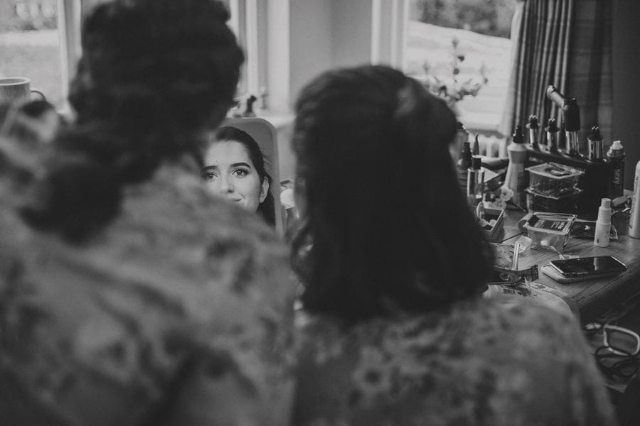 Bridesmaids sat next to each other at the side of a large wooden table looking into a small mirror