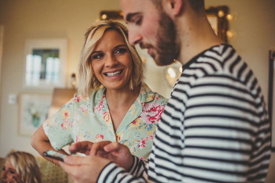 One of the bridesmaids stands in the kitchen and smiles at a man using a mobile phone