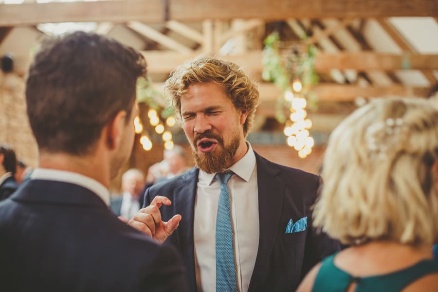 A wedding guest closes his eyes and holds his thumb and finger together as he chats to a man and lady