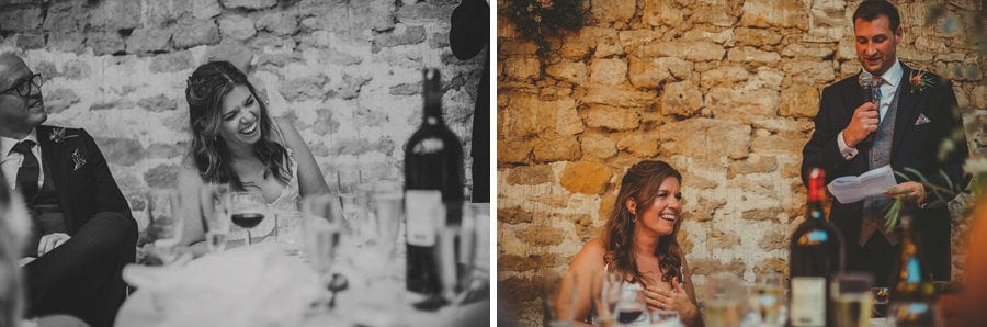 The groom delivers his speech to the wedding party and the bride sits at the table and laughs