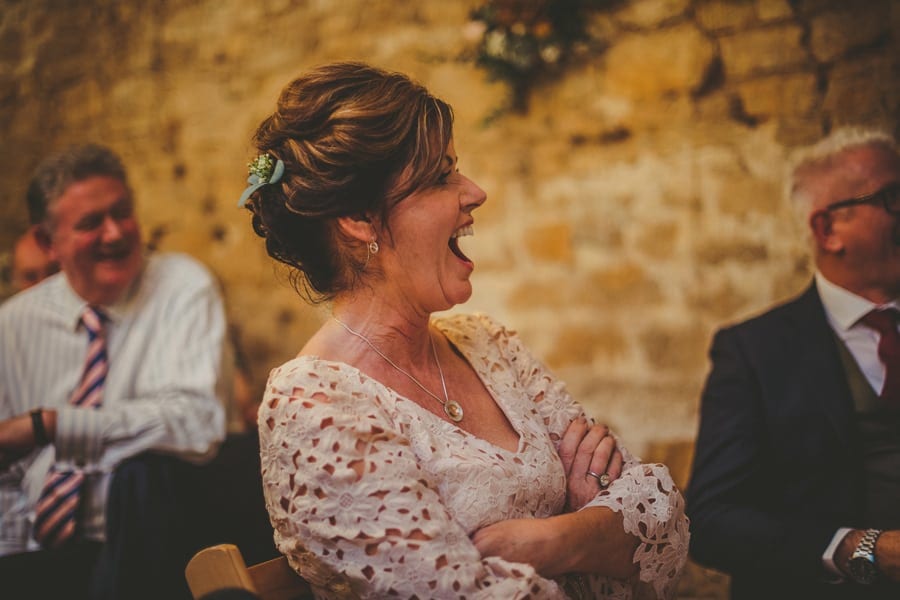 The brides mother sits at the table with her arms crossed and laughs