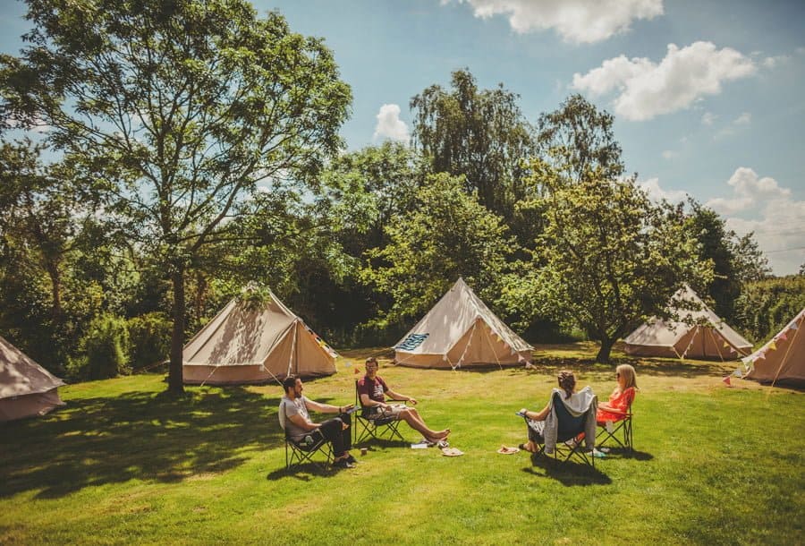 Wedding guests sit in camping chairs and sunbathe on the lawn at Mill farm