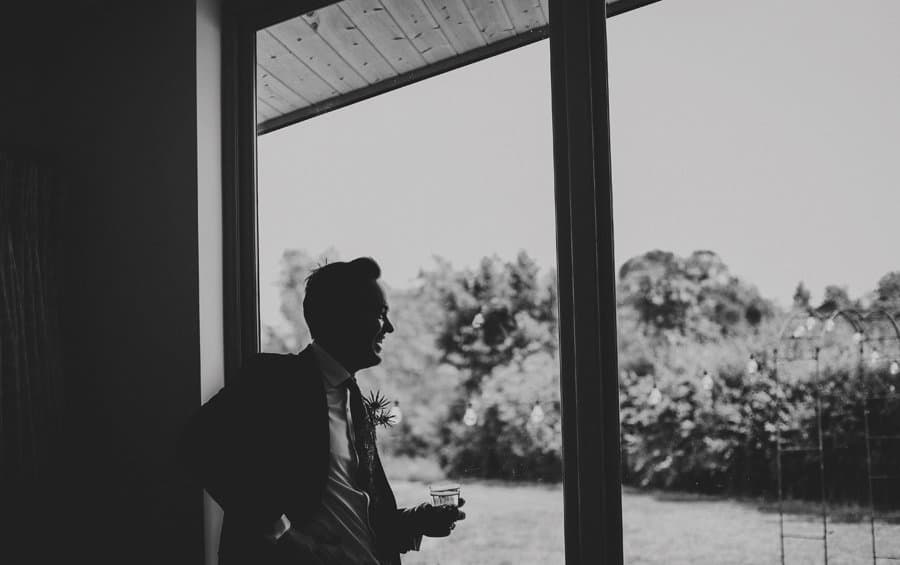 An usher holds a glass of whisky and looks out of the window in his apartment