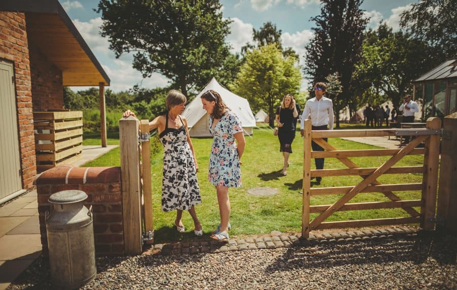 Wedding guests stand next to a large wooden gate in the courtyard at Mill farm