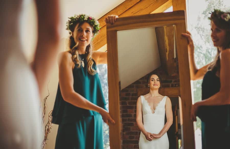 The bridesmaids hold up a large mirror as the bride looks at herself in her dress