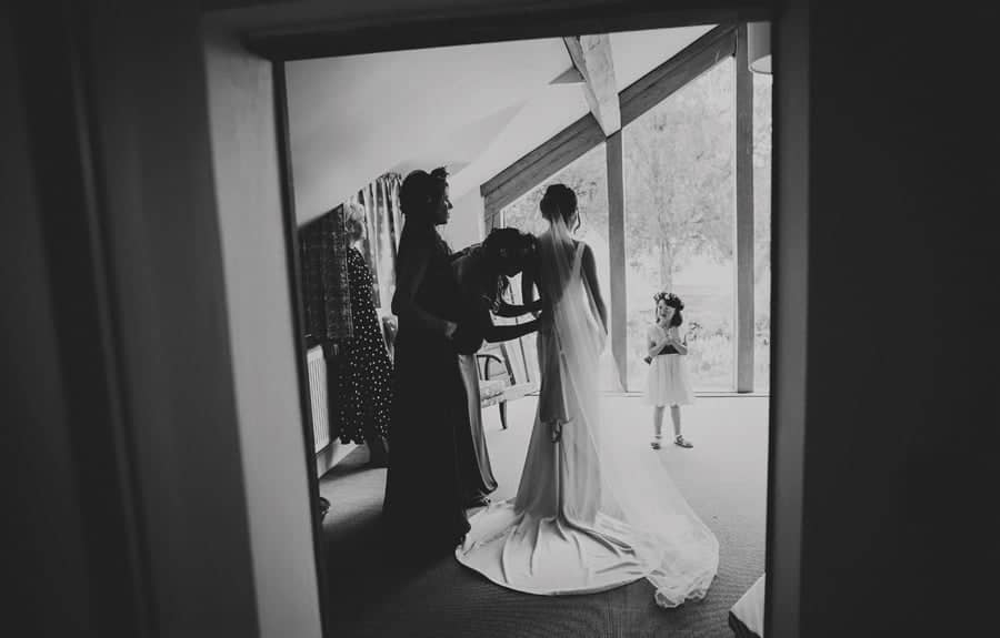 Bridesmaids fasten the back of the brides dress as the flowergirl stands and watches on