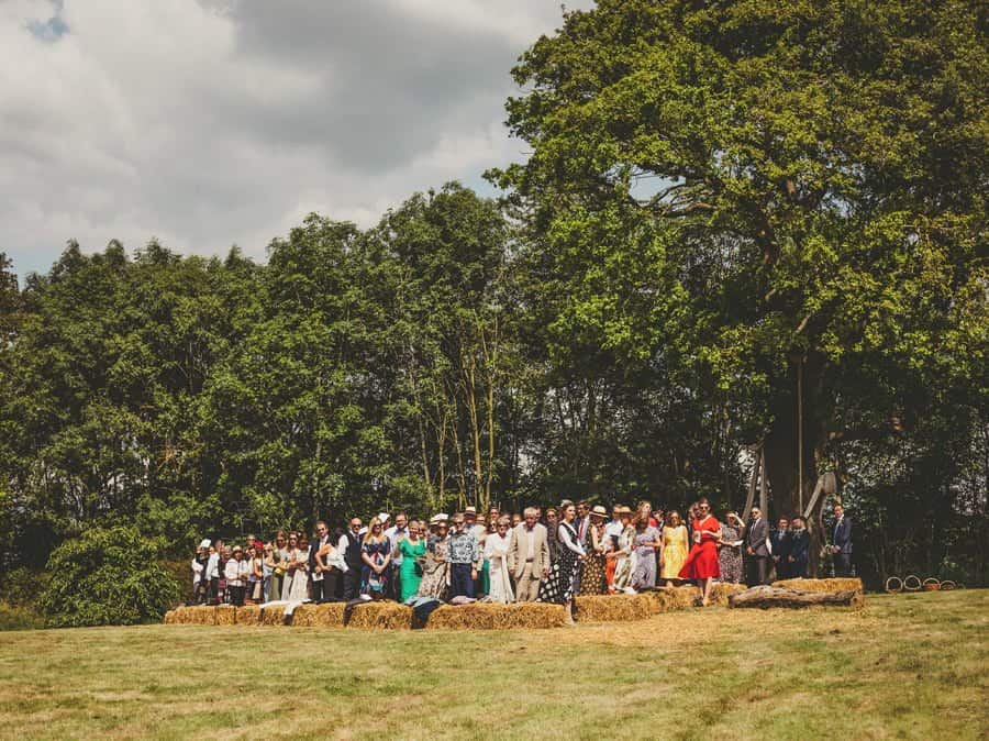 Wedding guests stand and watch the bride and her bridesmaids walking towards them