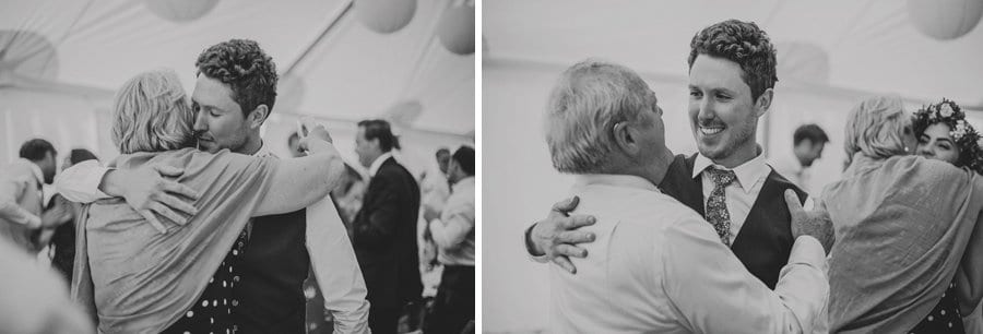 The groom hugs the brides mother and the brides father in the marquee