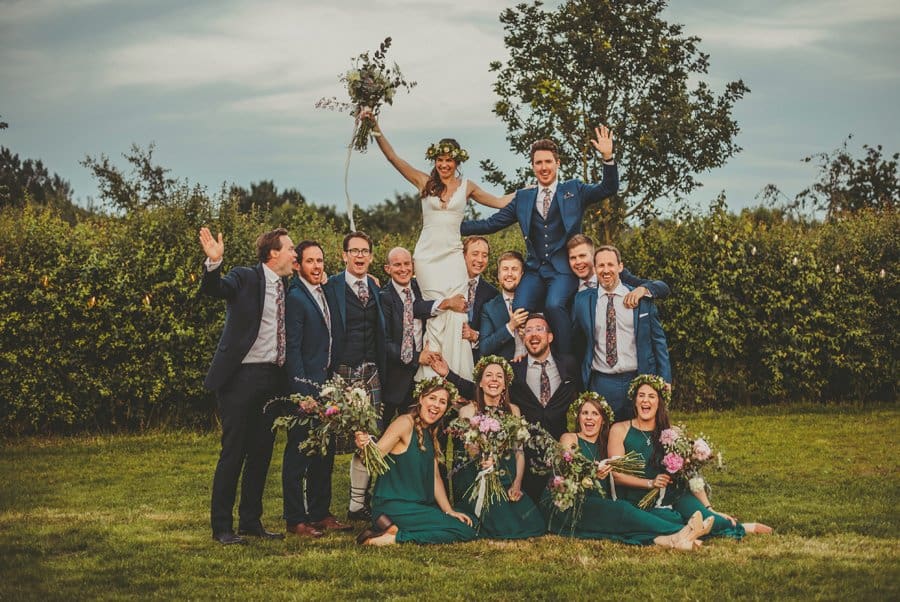 The bride and groom with their ushers and bridesmaids pose for a photograph on the lawn at Mill farm