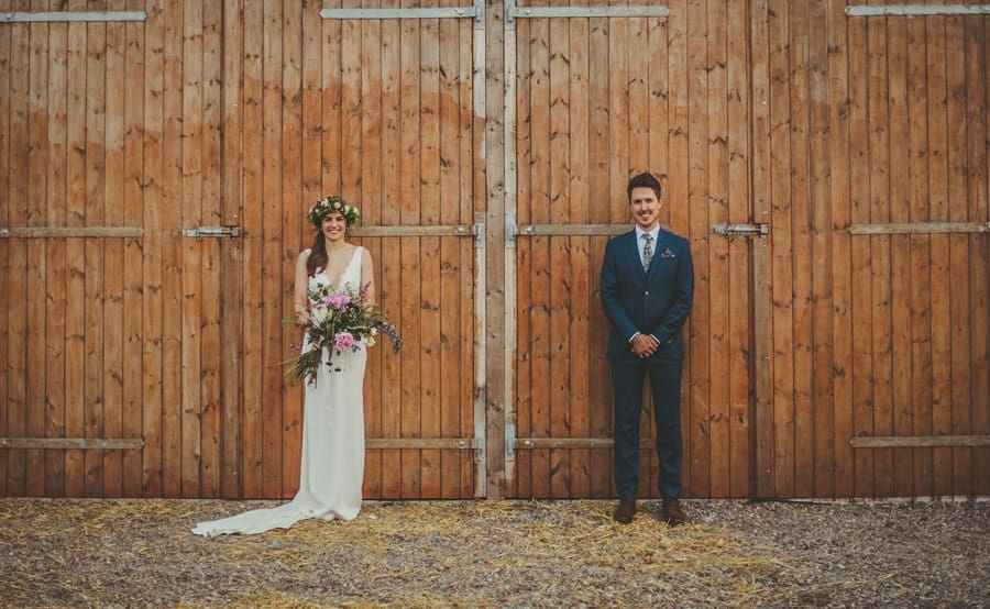 The bride and groom pose for a photograph stood next to the barn doors
