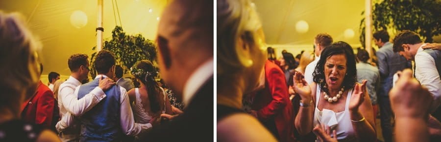 A friend of the groom places his arm over the grooms shoulder and a lady claps her hands on the dancefloor