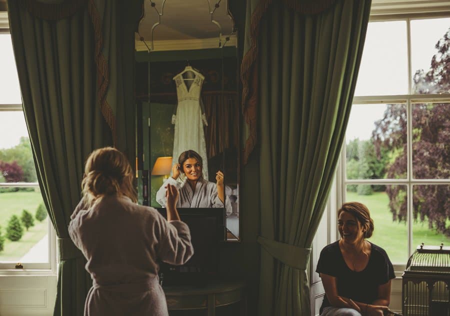 The brides sister looks in the mirror and laughs as she shares a joke with a friend