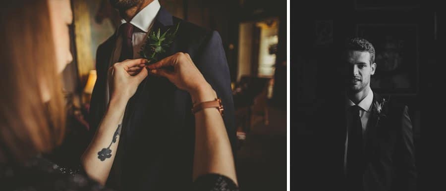 The groom poses for a photograph next to a window and a staff member places a flower on the lapel of the grooms suit jacket